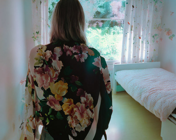 Person in floral kimono standing in bright room with white bedsheets and floral curtains