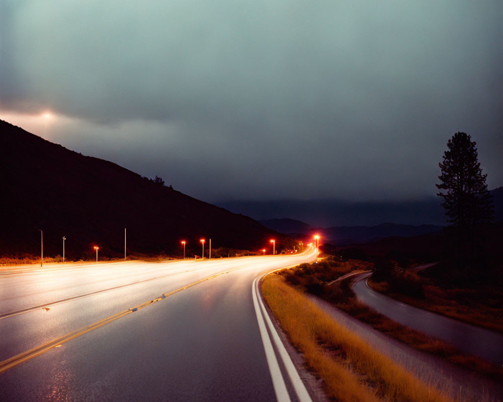 Twilight scene: Wet winding road with car light streaks & stormy clouds