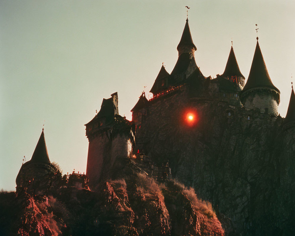 Medieval-style castle on rocky cliff at sunset with sun flare
