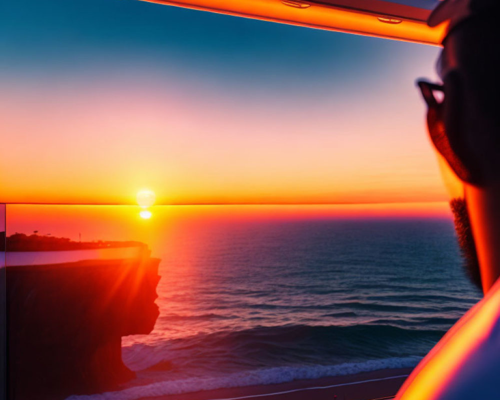 Silhouette person admiring vibrant ocean sunset through window frame