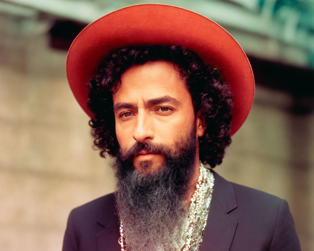 Bearded man in red hat with gold necklace gazes at camera