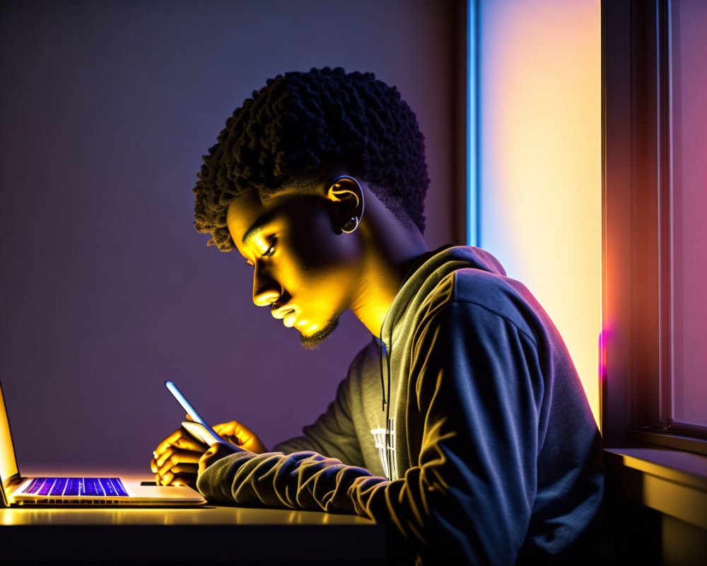 Young person working at laptop with purple and orange lighting.