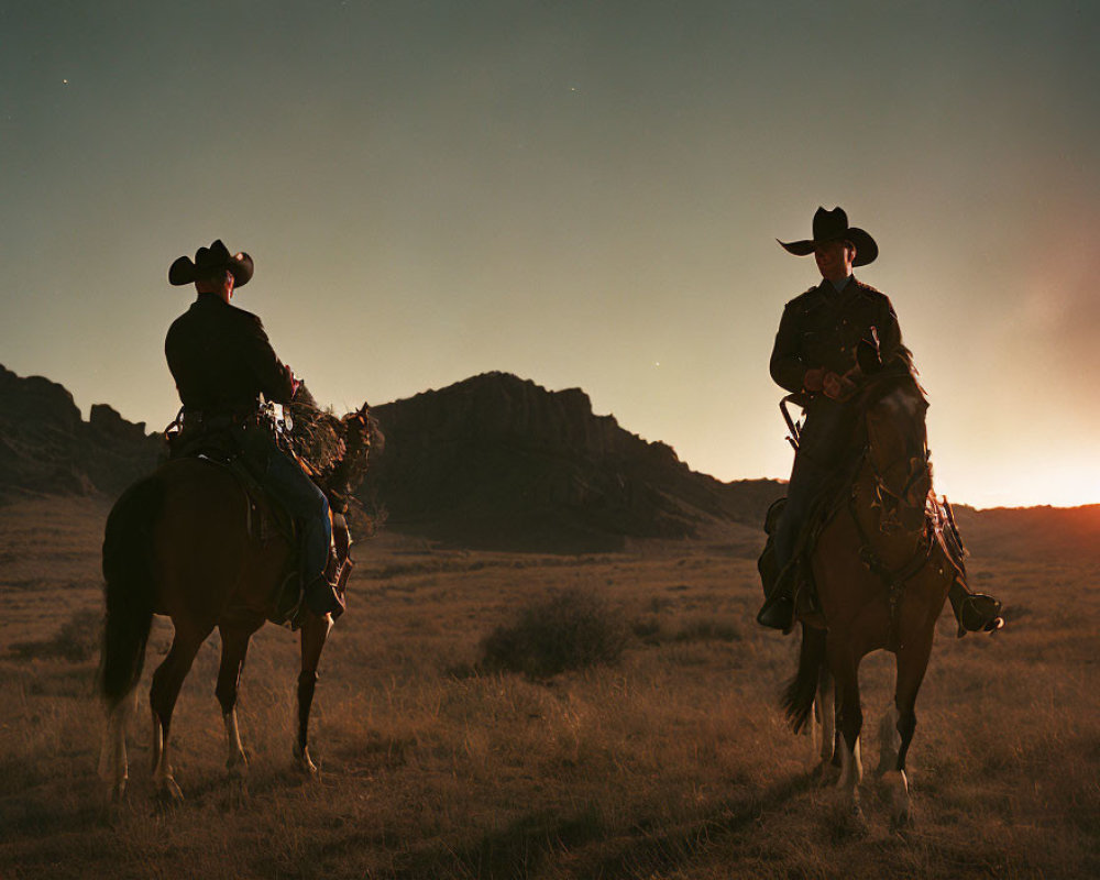 Two horseback cowboys against rolling hills at dusk
