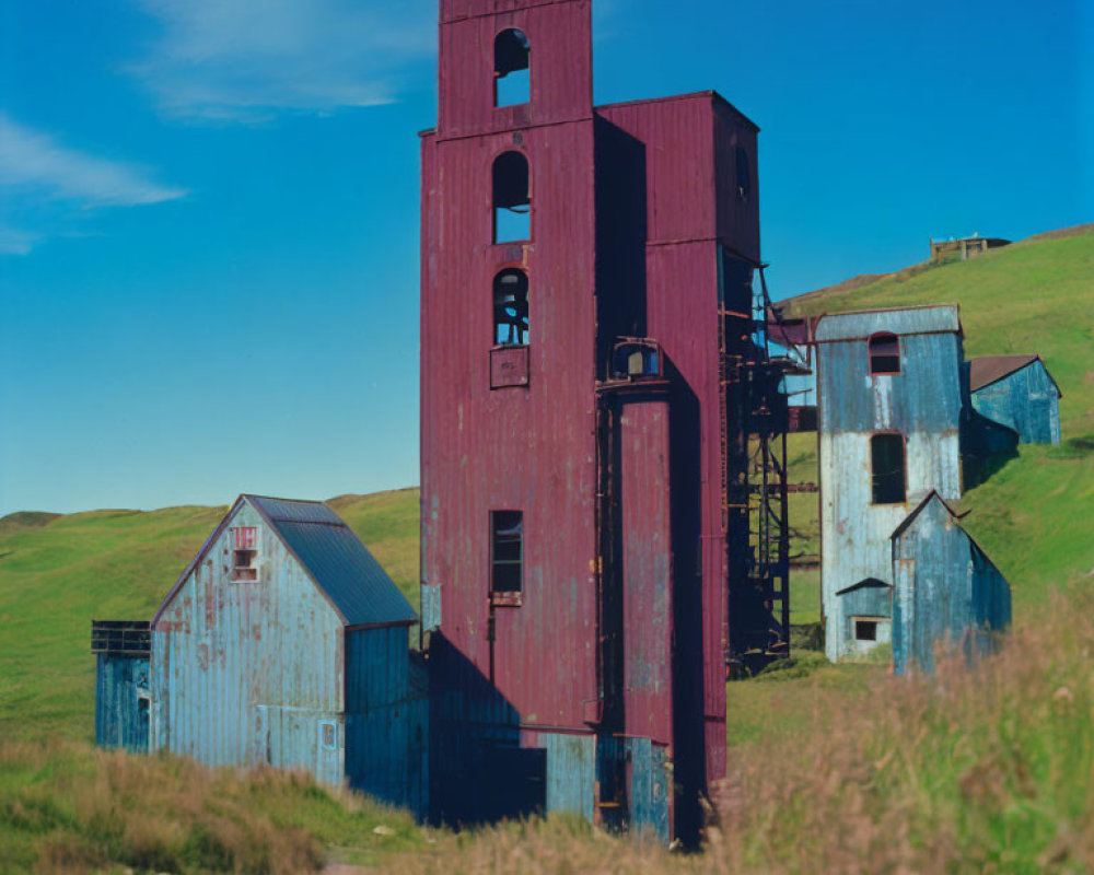 Tall Red Mining Headframe and Blue Building with Green Hills Background