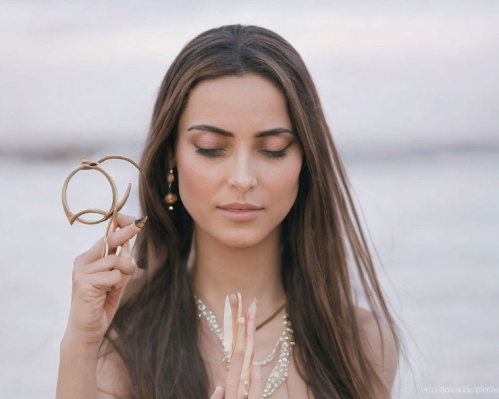 Dark-haired woman holding glasses gazes serenely at beach.