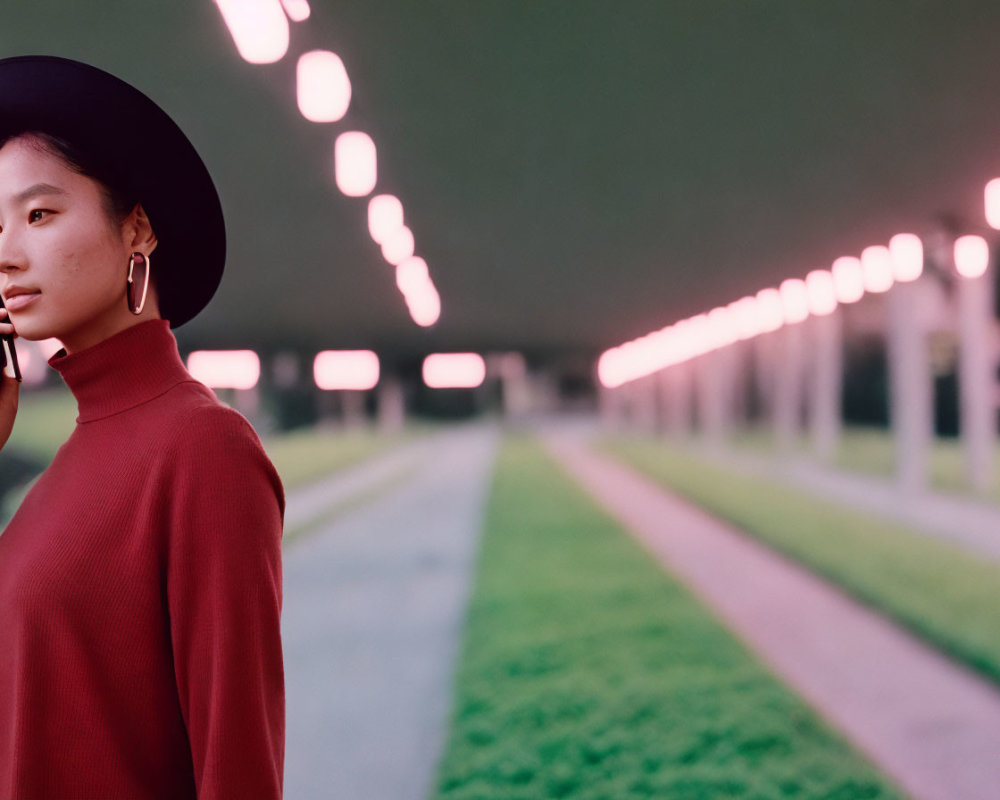 Woman in Red Turtleneck and Black Hat Standing Under Twilight Lights beside Grass Path