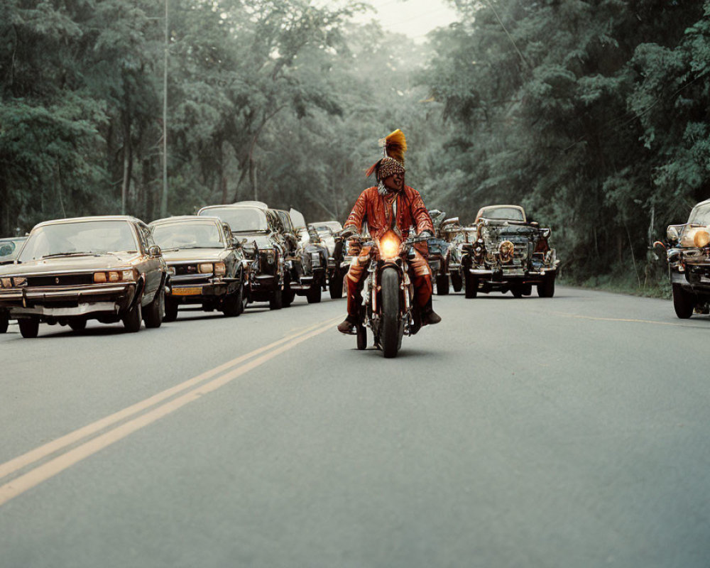 Person in traditional attire leads classic cars on road through forest.