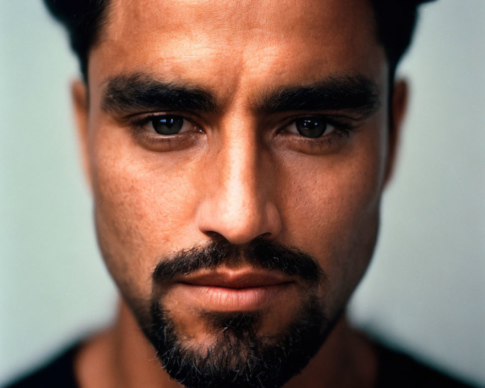 Intense dark-haired man with beard and clear skin in close-up portrait