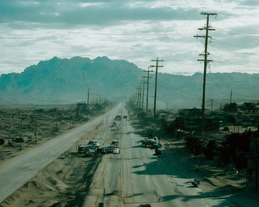 Scenic desert road with telephone poles and mountains under cloudy sky