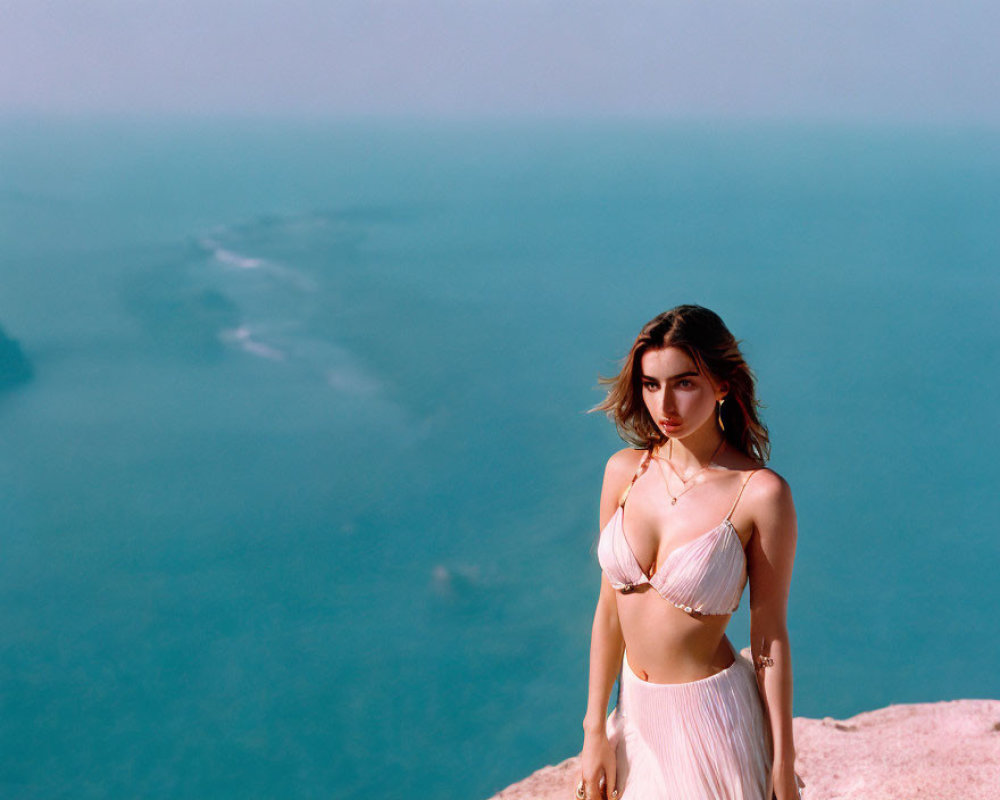 Person standing on cliff overlooking vast water under clear sky