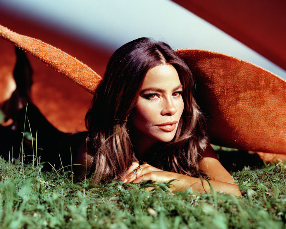 Woman in wide-brimmed orange hat lying on grass with red background