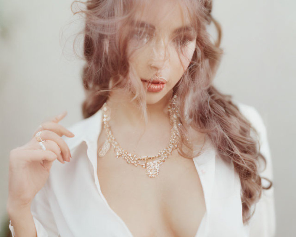 Tousled hair woman in white blouse with delicate necklace gazing seductively