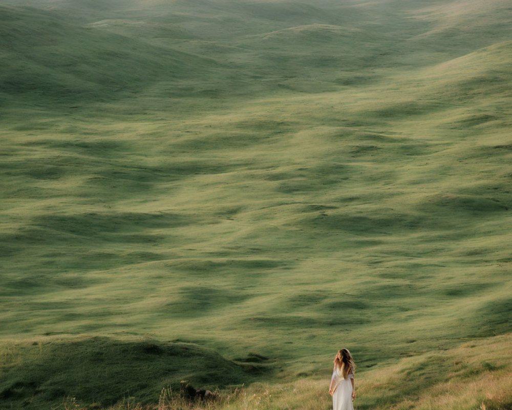 Person in White Outfit Amid Vast Green Hills
