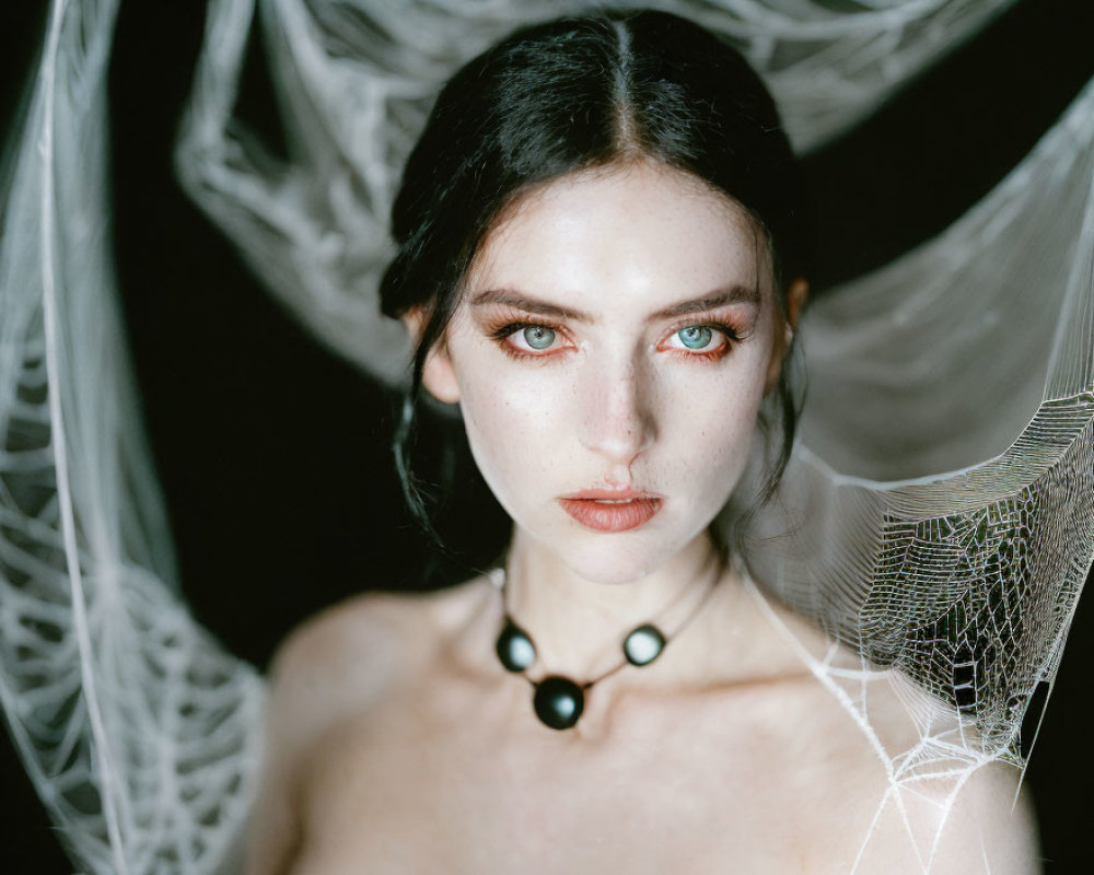 Pale-skinned woman with blue eyes and dark hair in gauzy fabric and choker.