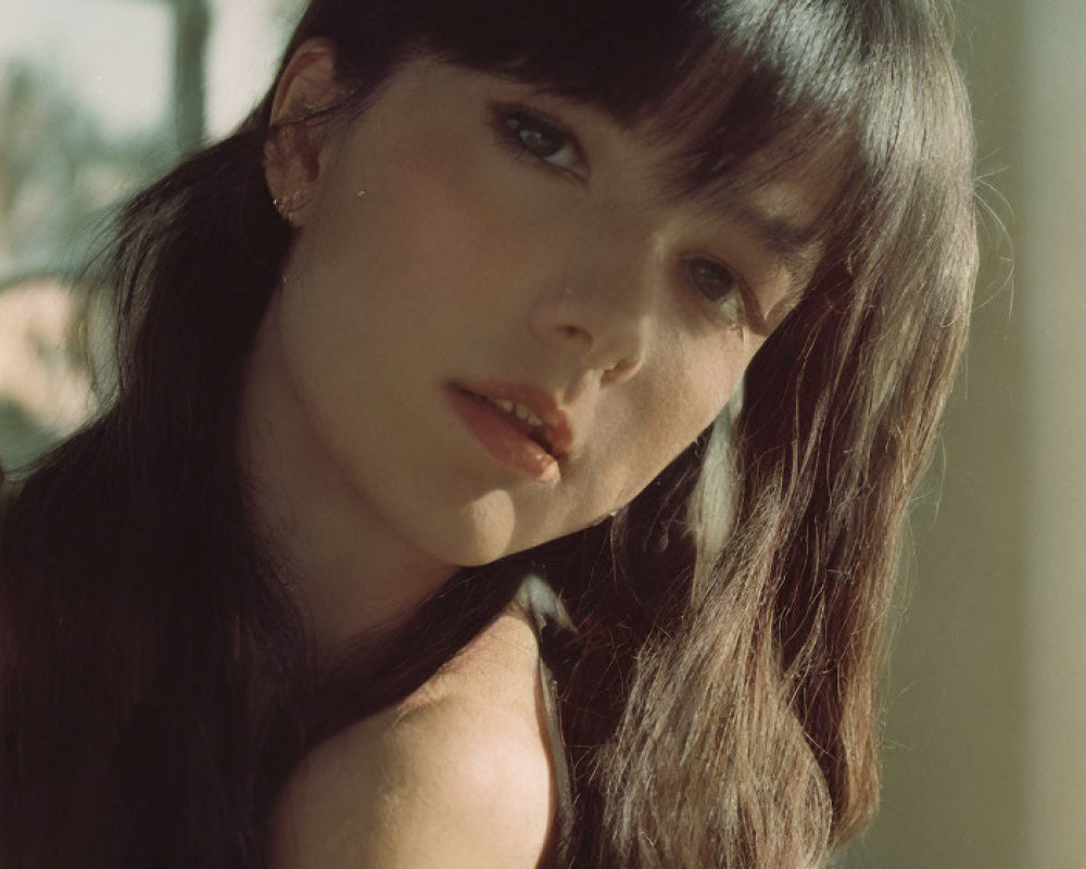 Portrait of woman with long dark hair and bangs under sunlight.