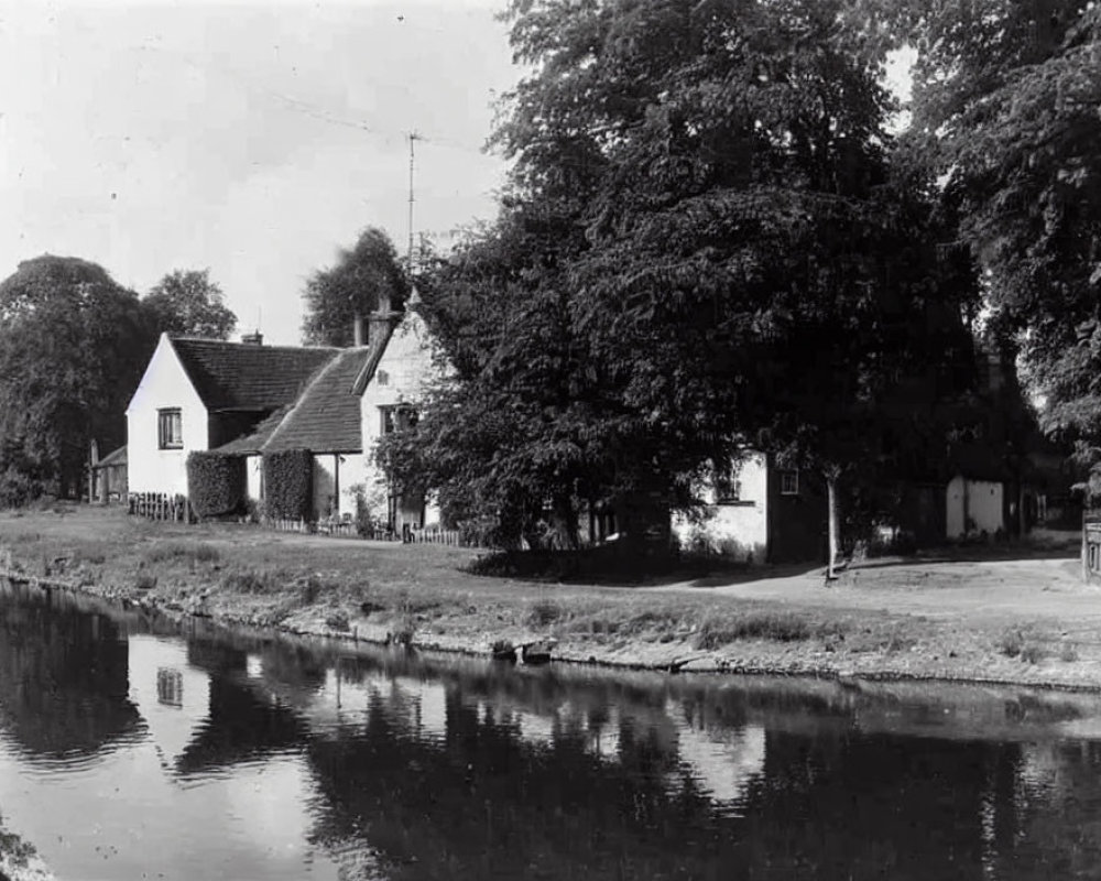 Tranquil black and white scene: Thatched-roof cottages by calm river