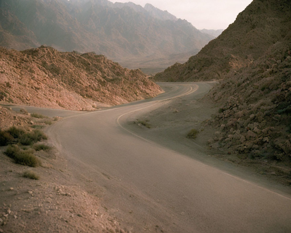 Winding road in rugged mountain landscape under subdued sky