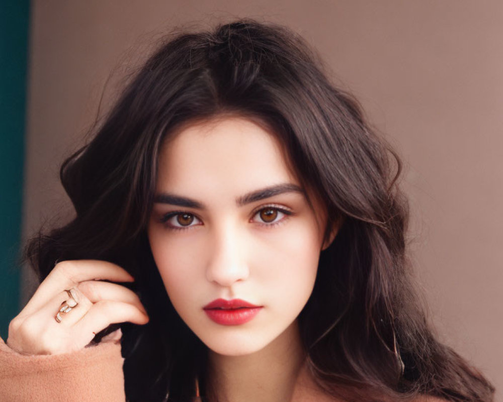 Portrait of woman with dark hair, bold eyebrows, red lipstick, beige coat, delicate necklace on blue