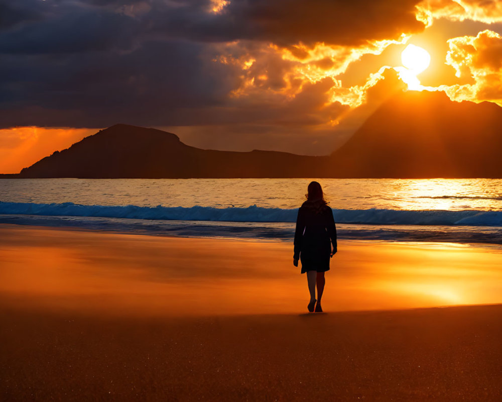 Solitary figure on beach watching vibrant sunset with sunbeams and silhouetted mountains
