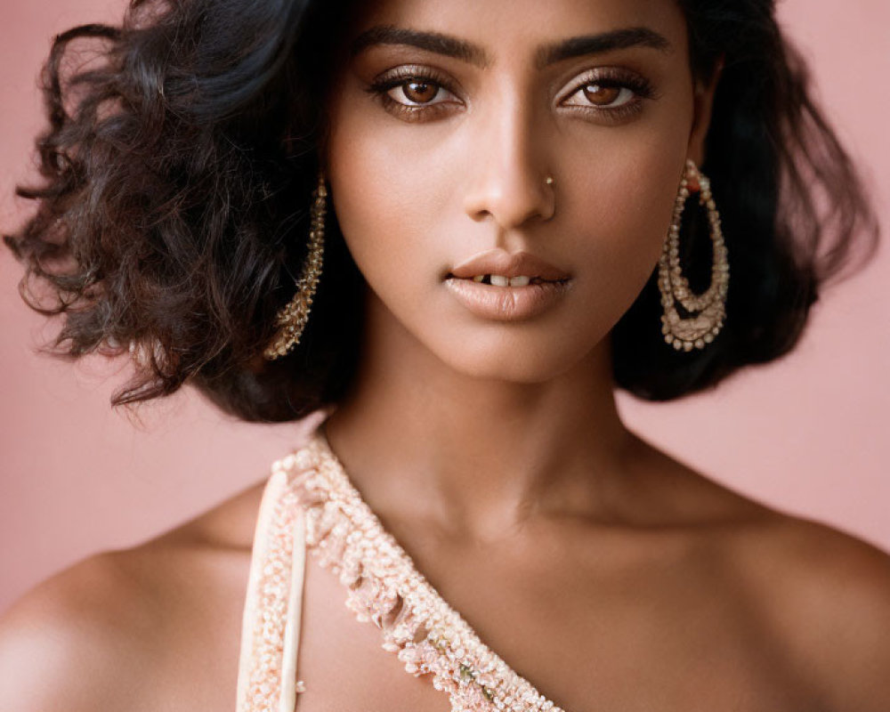 Dark-haired woman in golden jewelry and peach outfit gazes intently.