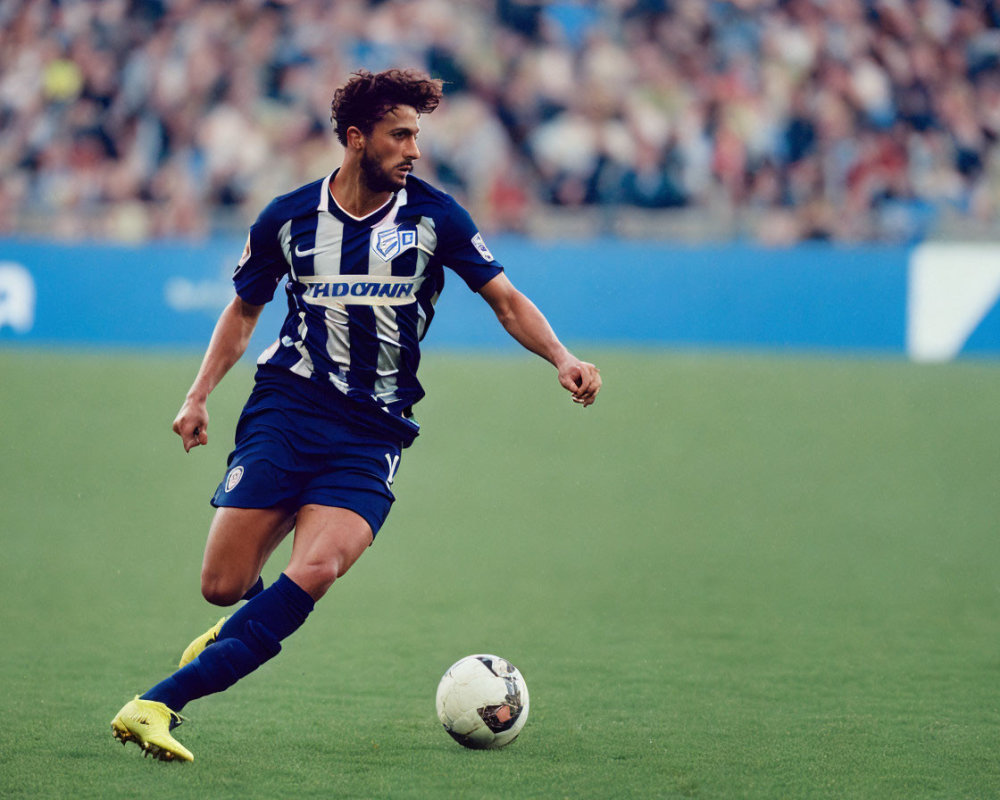 Soccer player dribbling ball on pitch with stadium spectators.
