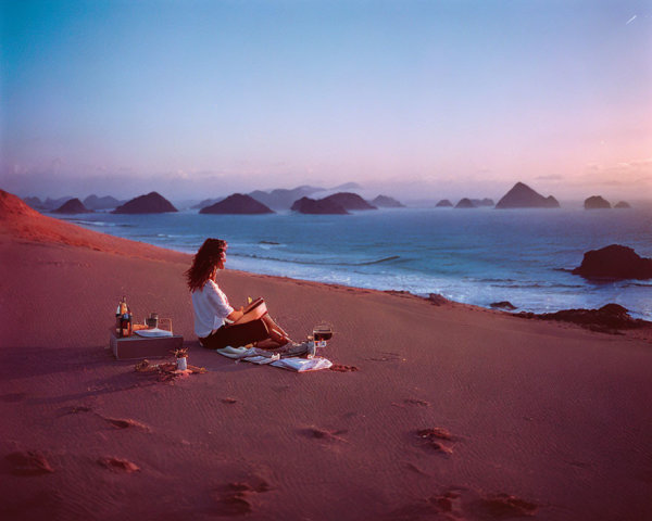 Person enjoys sunset picnic on sandy beach with ocean view