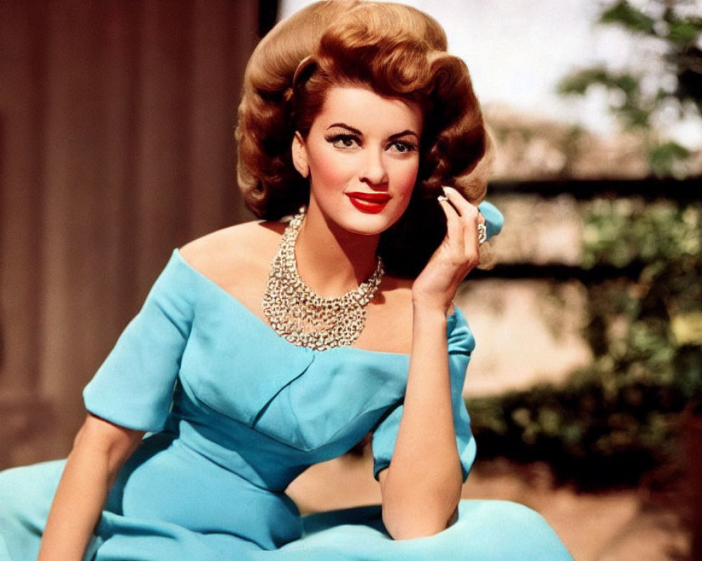 Blonde woman in blue dress with elaborate necklace sitting down